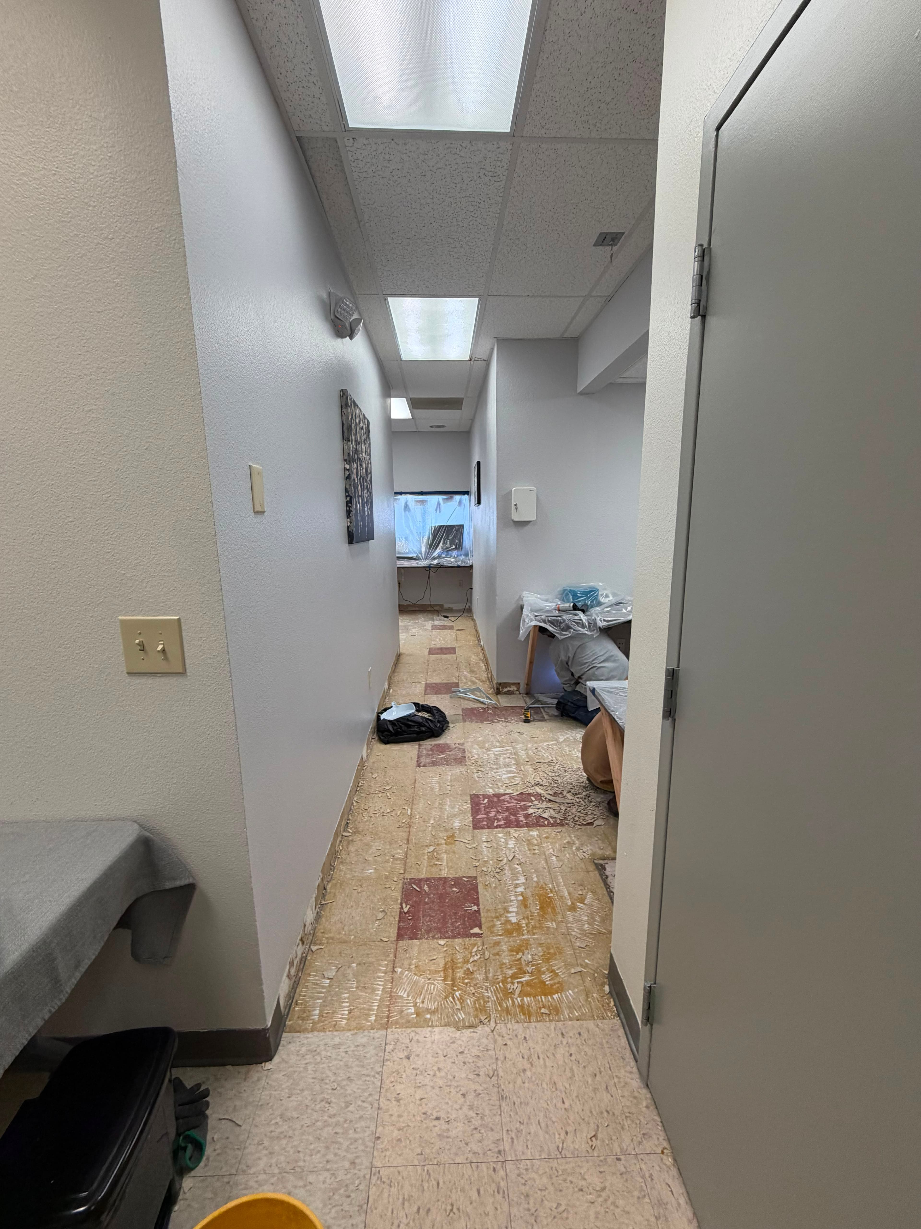 Workstations and casework sealed under plastic sheeting and taped off before flooring demolition begins in an occupied medical office corridor in El Paso.