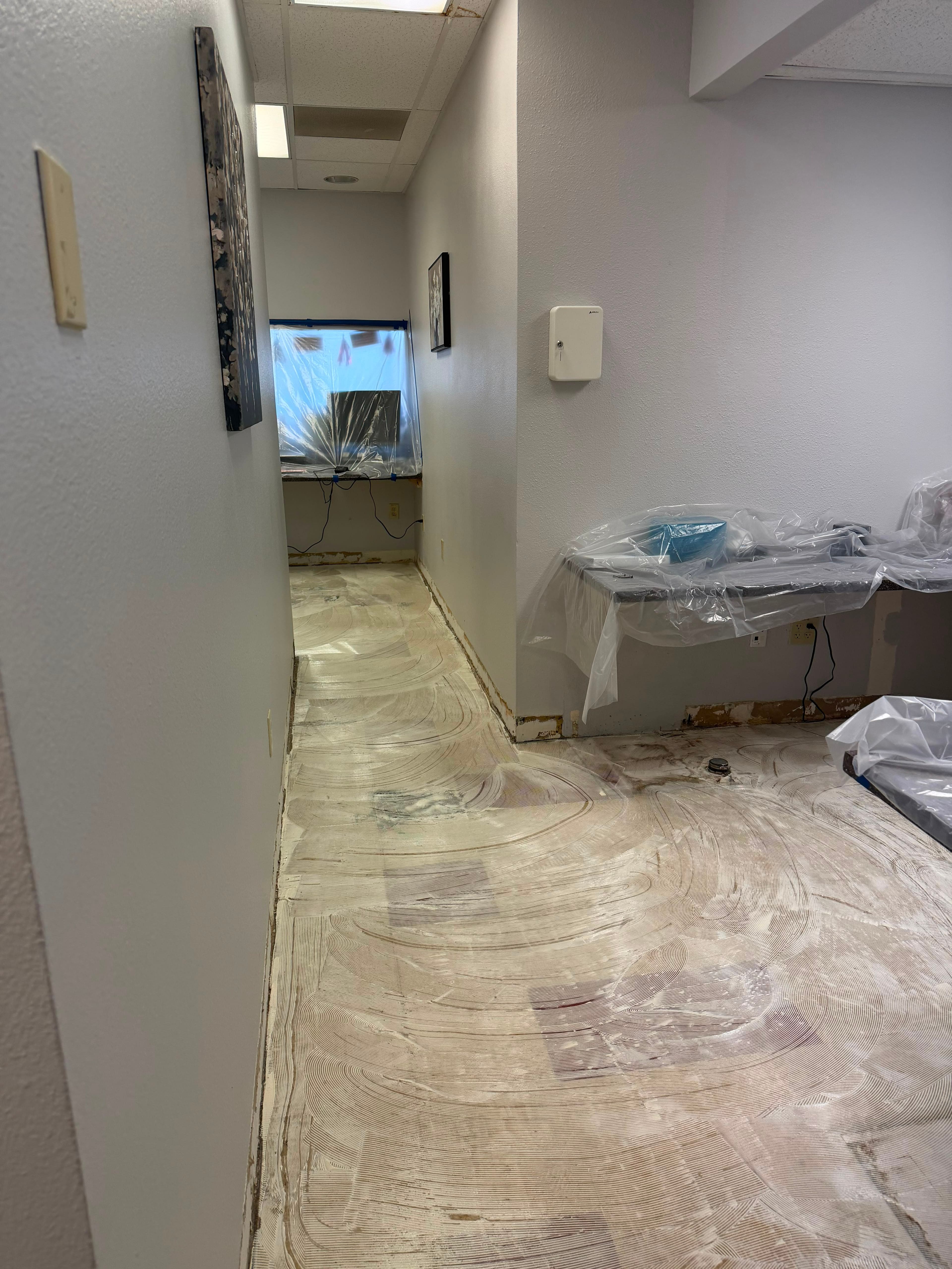 Concrete subfloor skim coated flat with leveling compound in swirled trowel passes after old adhesive removal, prepared for new flooring.